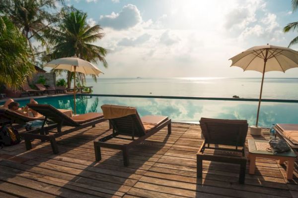 A serene poolside view with loungers and umbrellas, overlooking an ocean under a bright sun and a clear sky.