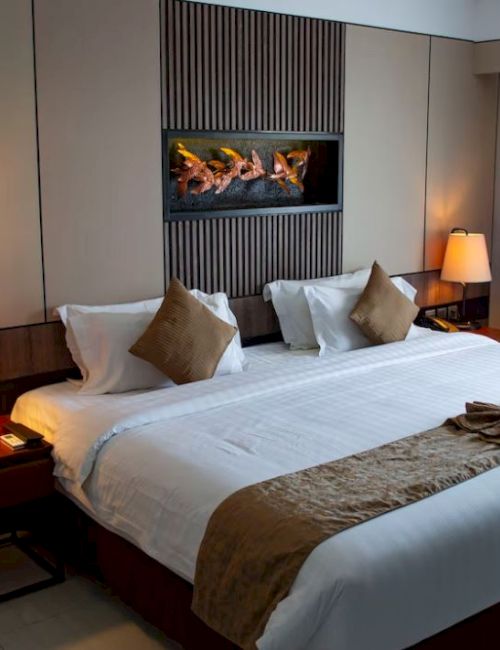 A neatly arranged hotel room with a large bed, decorative pillows, bedside tables with lamps, and a folded towel on the bed.