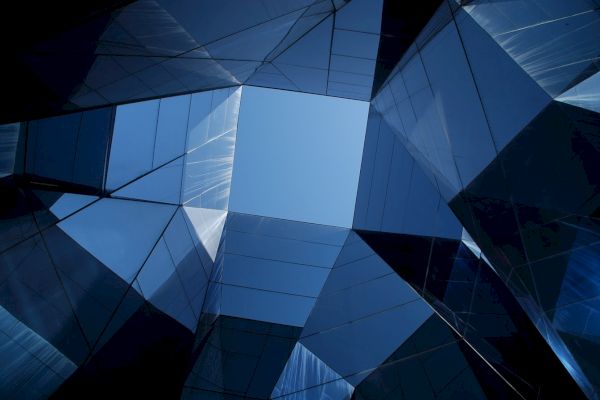 Abstract view of skyscraper architecture, looking upwards at mirrored glass panels reflecting the sky and each other.