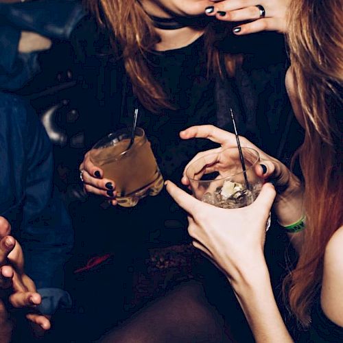 People are enjoying drinks and conversation in a social setting, with visible smiles and gestures, creating a lively and fun atmosphere.