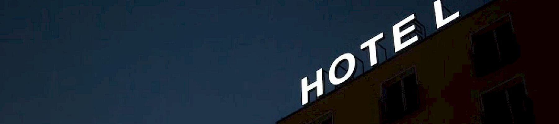 The image shows the corner of a building at night with a sign that says "HOTEL" in white letters against a dark sky.