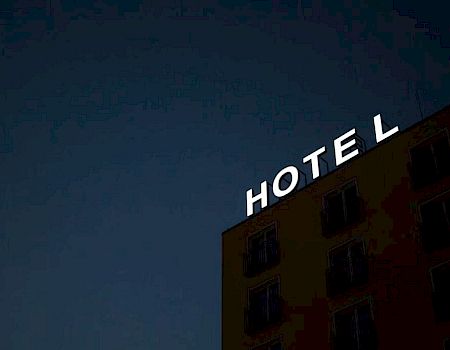 The image shows the corner of a building at night with a sign that says "HOTEL" in white letters against a dark sky.