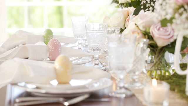 A beautifully set table with floral arrangements, glassware, and decorated eggs on plates, ready for a special occasion or celebration.