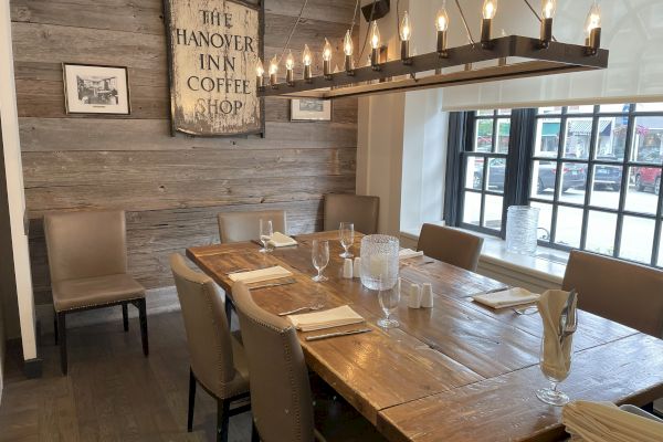 A rustic dining area with a wooden table, leather chairs, and a vintage sign reading "The Hanover Inn Coffee Shop."
