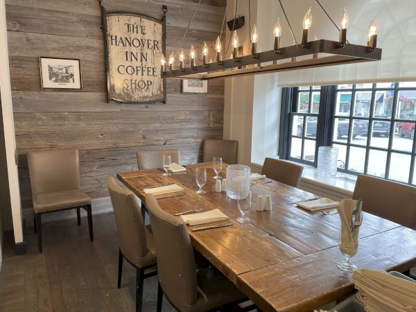 A rustic dining area with a wooden table, leather chairs, and a vintage sign reading "The Hanover Inn Coffee Shop."