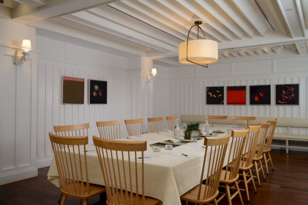 A dining room with a long table, wooden chairs, artworks on walls, and soft lighting creating a cozy atmosphere.
