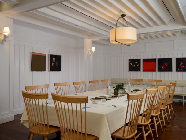 A dining room with a long table, wooden chairs, artworks on walls, and soft lighting creating a cozy atmosphere.