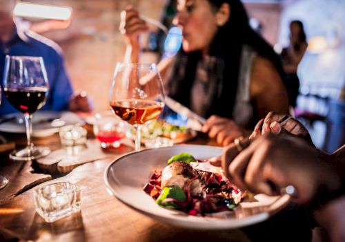 People dining at a table with wine glasses and a plate of food, focusing on a social meal setting.