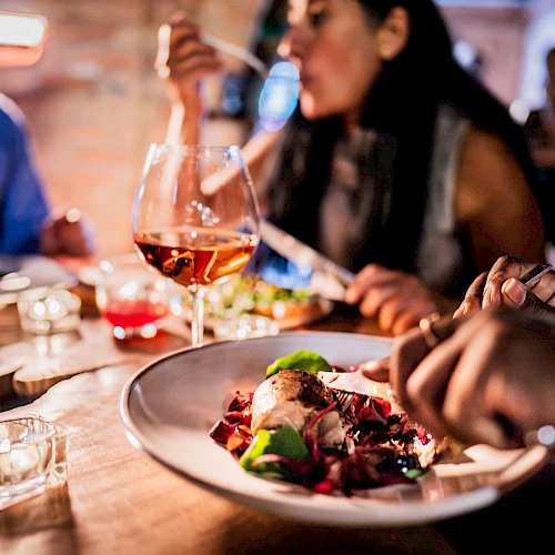 People dining at a table with wine glasses and a plate of food, focusing on a social meal setting.