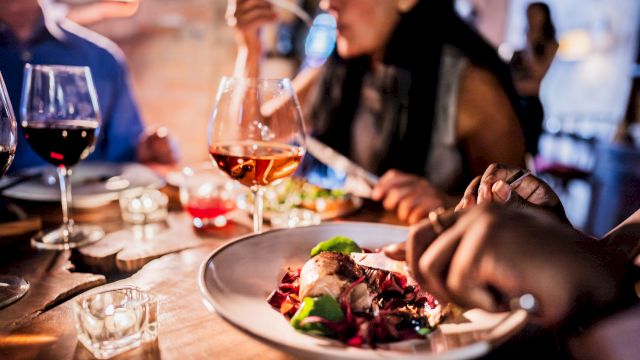 People dining at a table with wine glasses and a plate of food, focusing on a social meal setting.