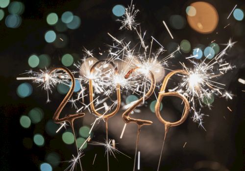 Sparkling 2026-shaped sparklers are lit against a dark, bokeh-filled background, creating a festive atmosphere.