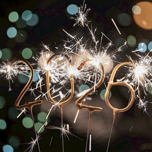 Sparkling 2026-shaped sparklers are lit against a dark, bokeh-filled background, creating a festive atmosphere.
