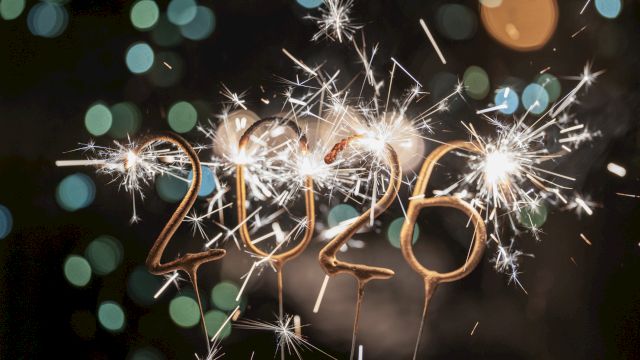 Sparkling 2026-shaped sparklers are lit against a dark, bokeh-filled background, creating a festive atmosphere.