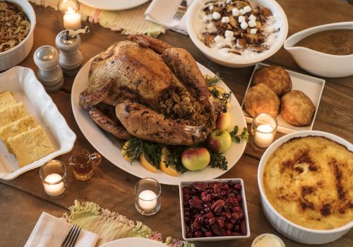 A Thanksgiving feast with roast turkey, stuffing, mashed potatoes, cranberry sauce, bread, and candles on a wooden table.