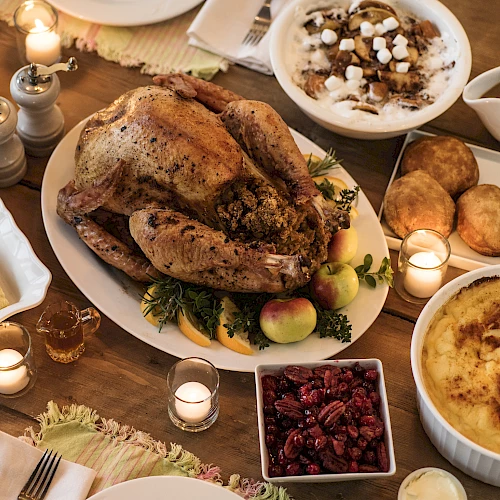 A Thanksgiving feast with roast turkey, stuffing, mashed potatoes, cranberry sauce, bread, and candles on a wooden table.