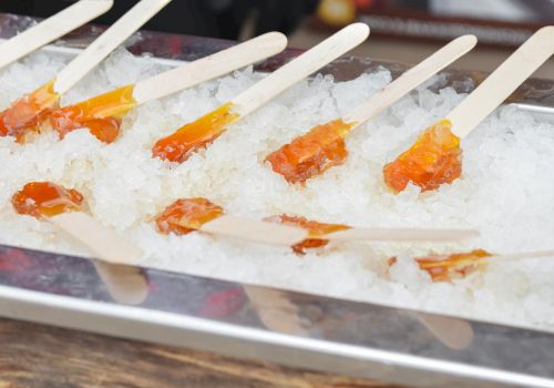 Sliced orange fruit on sticks, possibly mandarin or peach, served on ice in a metal tray, likely a cold fruit skewer bite.
