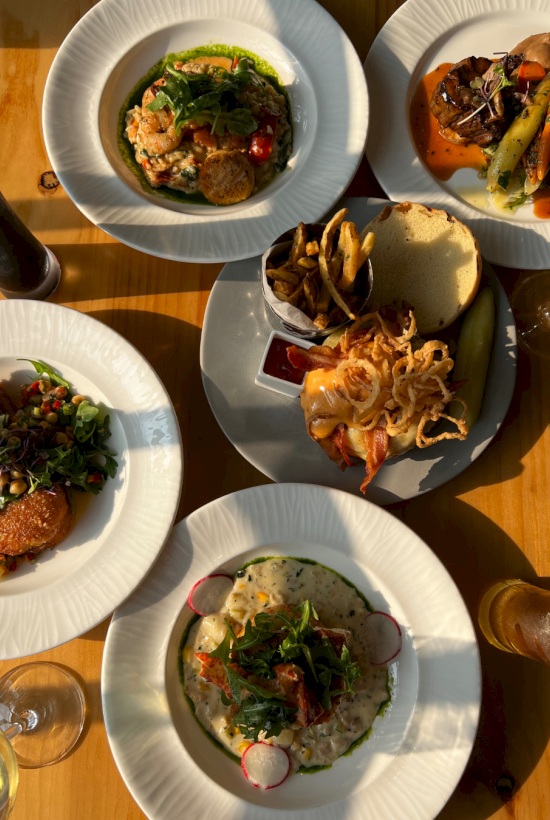 A table of plated brunch dishes: salads and soups with bread, fries, and mains, all served on white plates.