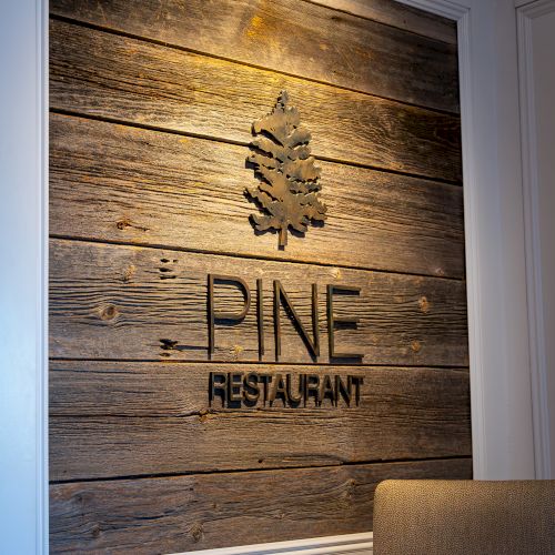 A rustic wood sign reading &ldquo;PINE RESTAURANT&rdquo; with a golden treeflake emblem inside a doorway.
