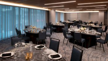 The image shows a decorated banquet hall with round tables, elegant table settings, and dim lighting, ready for an event.