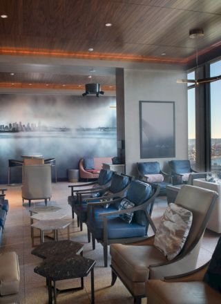 This image shows a modern lounge with comfortable seating, a cityscape mural, and large windows offering a view of the water and Ferris wheel.