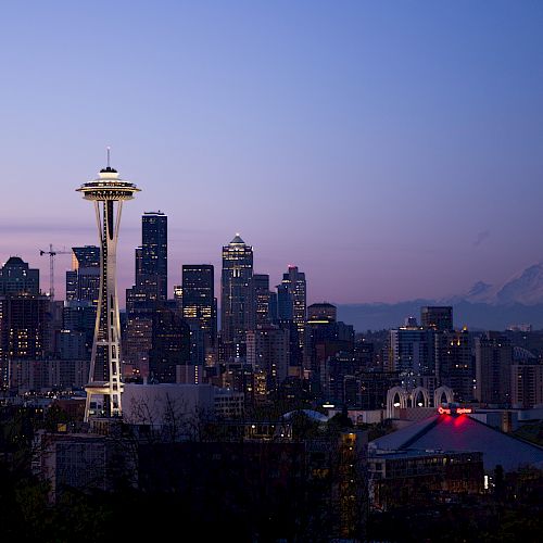 Seattle skyline at dusk with the Space Needle and Mount Rainier visible against a colorful sky.