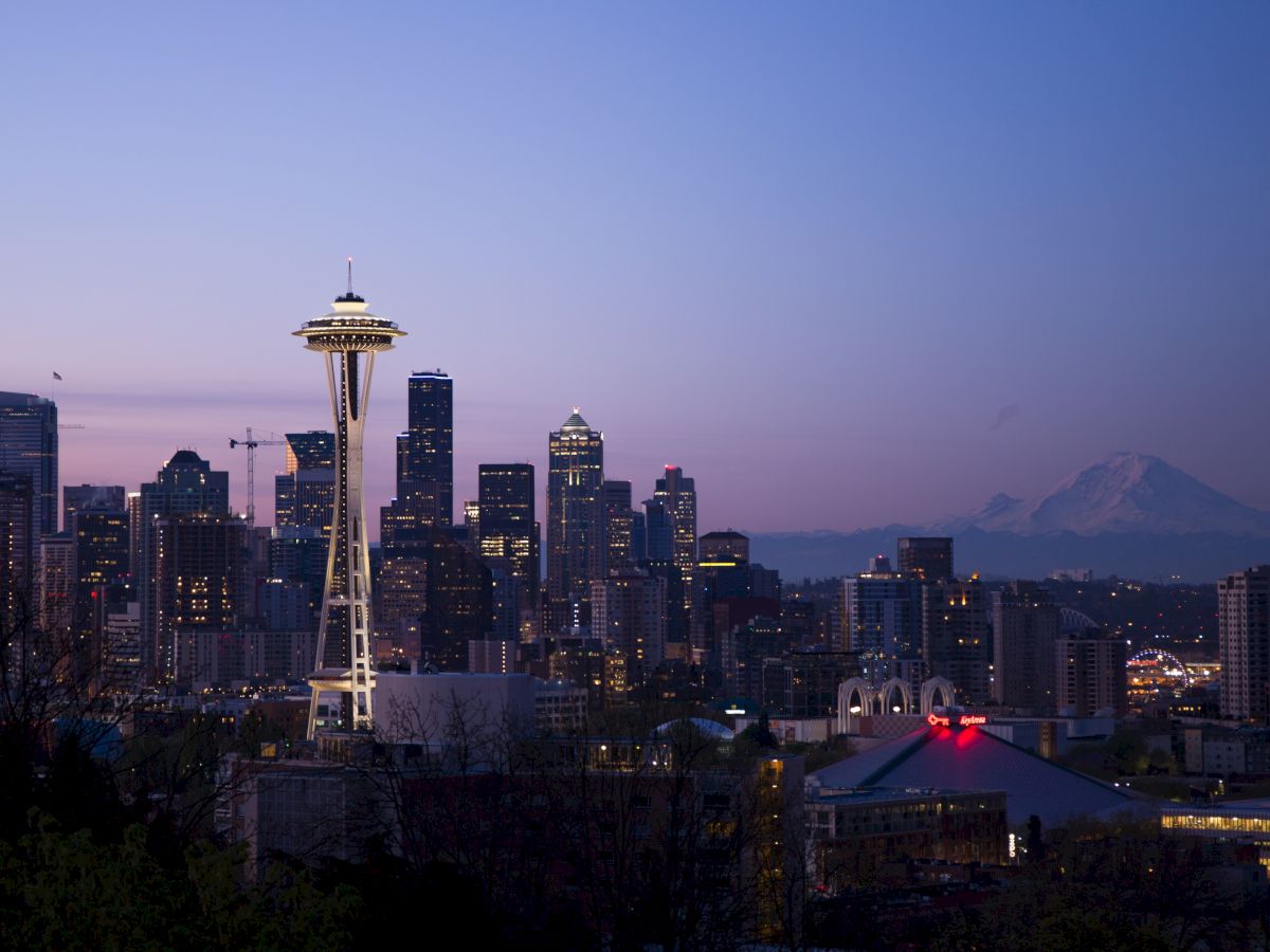 The image shows Seattle's skyline at dusk, featuring the Space Needle and Mount Rainier in the background, under a purple and blue sky.