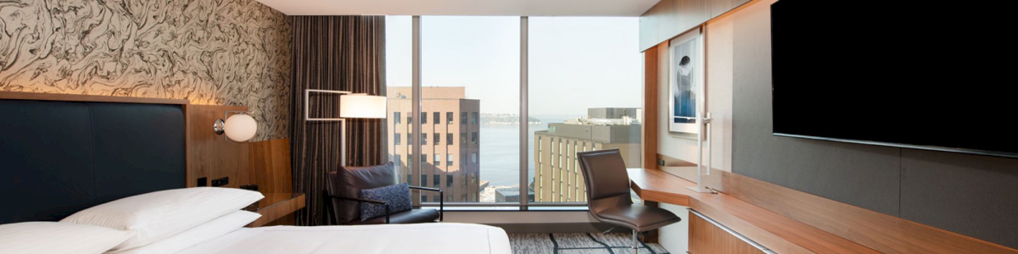 A modern hotel room with a large bed, wall-mounted TV, desk, chair, and a city view through large windows completes the scene.